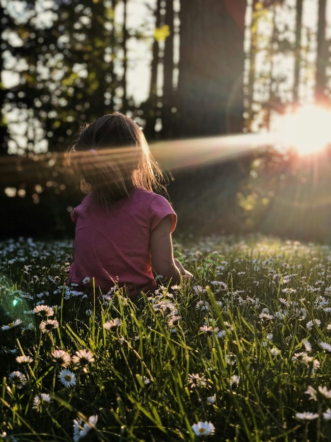 My family was enjoying some time on a hike in a wooded area.  The way the light was coming through the trees and across the grass and daisies was making me itch to capture the moment. 

I got down on my stomach in the grass to capture this photo of my daughter Ellie. All I had with me that day was my iPhone X which was still a champ for captuing the moment perfectly. I just love the way the end of the day sunlight was making her glow.  To me this photo perfectly captures summer, childhood, and my sweet girl, who shines brighter then the sun.